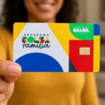 Pessoa sorrindo em um ambiente interno desfocado, segurando em primeiro plano um cartão colorido do programa Bolsa Família com chip visível e design geométrico em amarelo, azul, verde e vermelho.